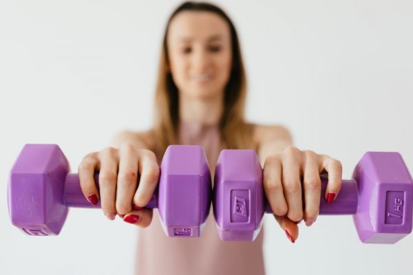 Defocused content young female doing bicep exercise with dumbbells during functional training in light studio